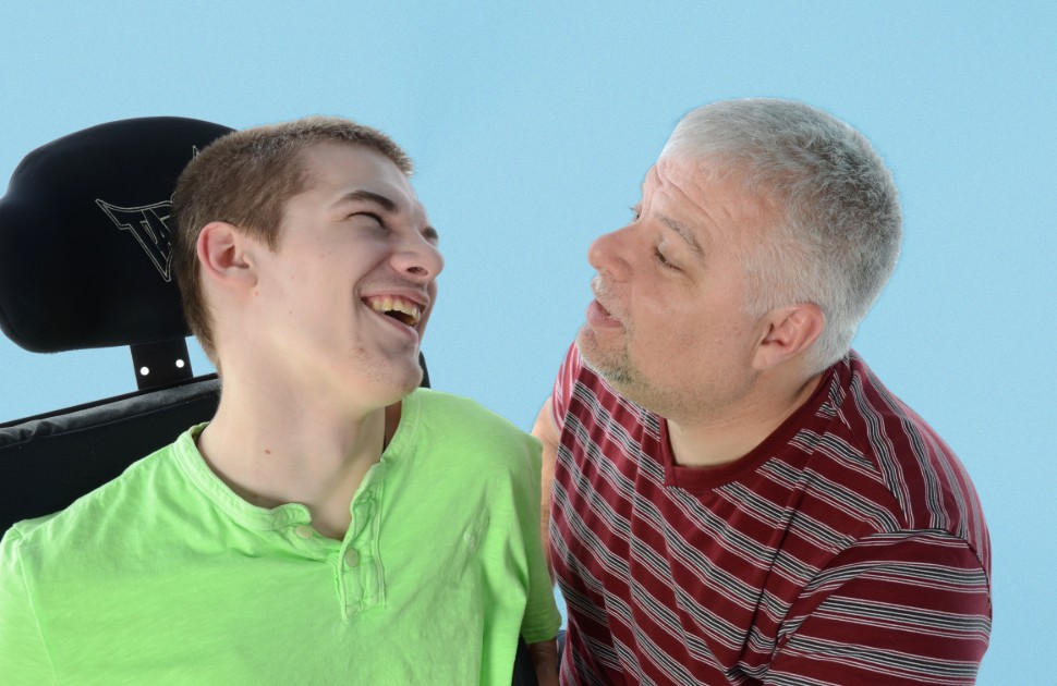 Boy in wheelchair and father smiling at each other