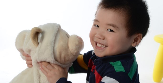 Child hugging a stuffed animal and smiling at the camera