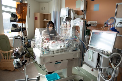 A NICU room, with a staff member helping a baby who is in an isolette.