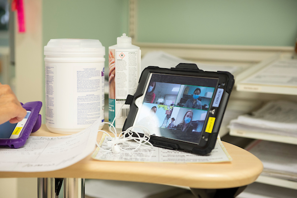 An iPad sitting on a desk, showing a Zoom call. Medical supplies such as Virox wipes are in the background